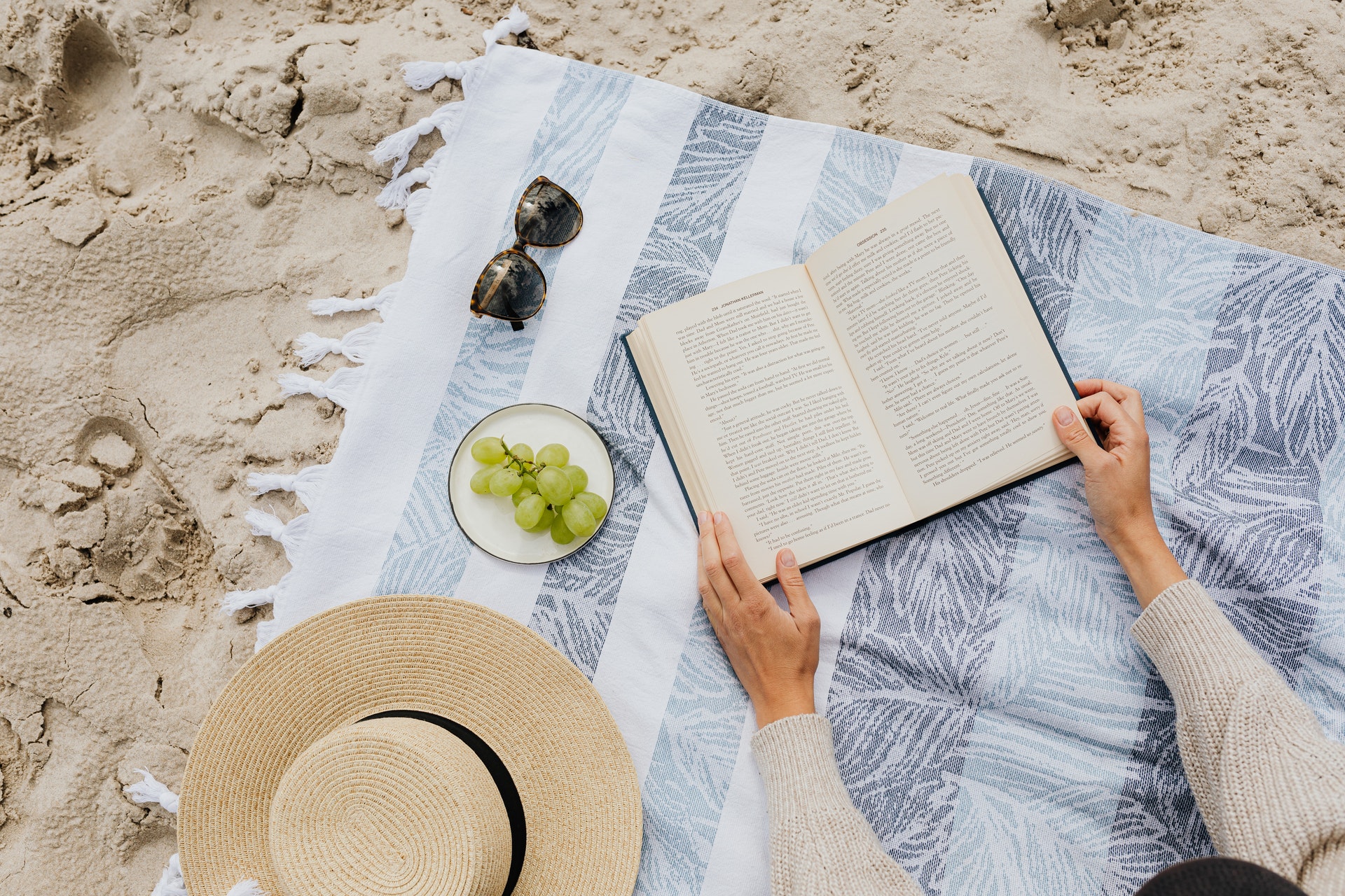 Person reading a book on a blanket over the sand